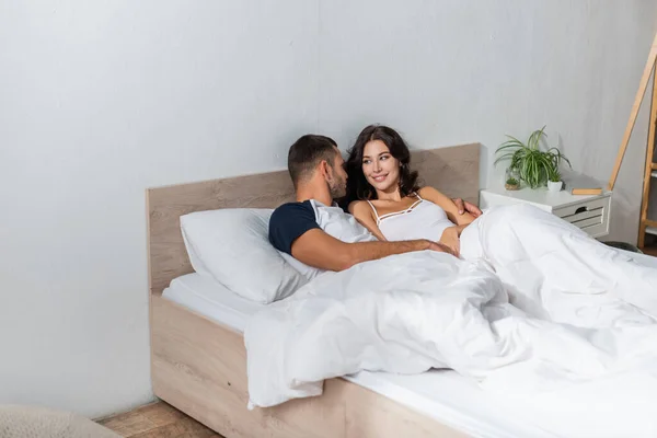 Bärtiger Mann umarmt positive Freundin zu Hause im Bett — Stockfoto