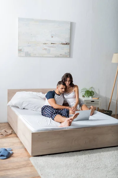 Couple in pajama holding hands near laptop on bed in morning — Foto stock