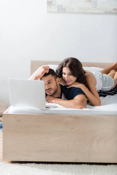 Woman lying on boyfriend near laptop on bed at home — Stockfoto