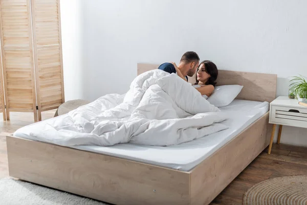 Bearded man kissing girlfriend on bed in morning — Stockfoto