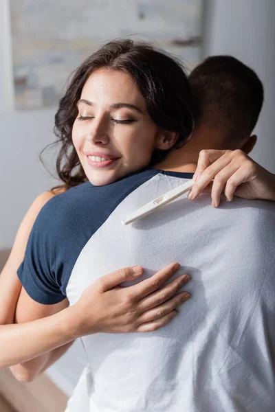 Positive woman holding pregnancy test and hugging boyfriend at home — Stockfoto