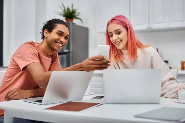 Happy loving multiracial couple in casual attires working at laptops and looking at smartphone — Stock Photo