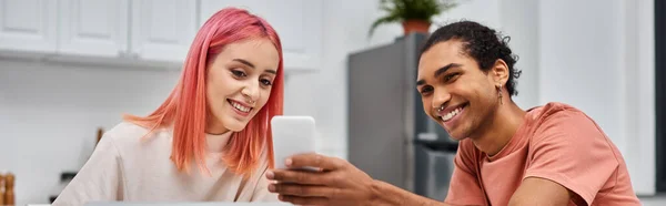 Loving multiracial couple in casual attires working at home and looking at smartphone, banner — Stock Photo