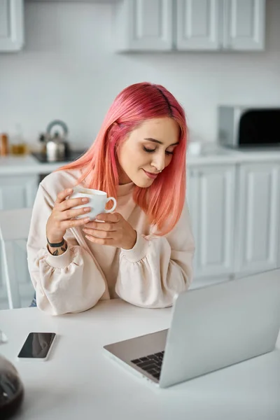 Séduisante femme élégante avec les cheveux roses travaillant à l'ordinateur portable boire du café chaud et détourner les yeux — Photo de stock