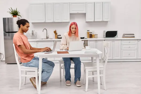 Attrayant travail dur couple interracial assis à la table dans la cuisine avec des ordinateurs portables, freelance — Photo de stock