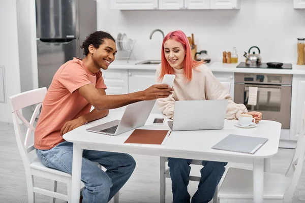 Allegro afro americano uomo in homewear mostrando qualcosa al telefono alla sua fidanzata attraente — Foto stock