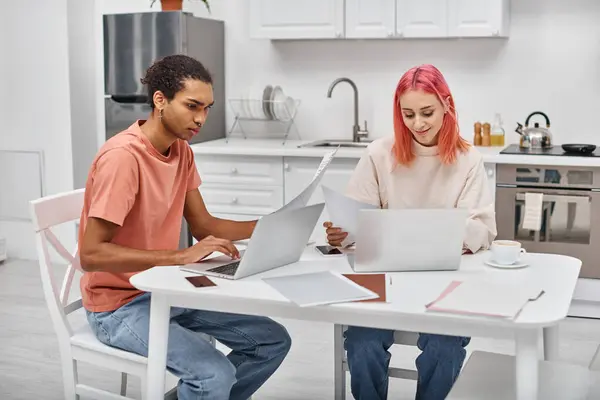 Beautiful young interracial couple in homewear working with paperwork and laptops in kitchen at home — Stock Photo