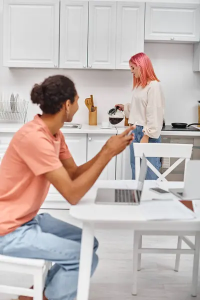 Focus on pink haired woman pouring coffee near her blurred african american boyfriend looking at her — Stock Photo