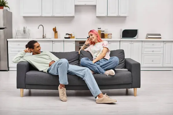 Bom olhar alegre casal interracial relaxante no sofá na sala de estar e sorrindo um para o outro — Fotografia de Stock