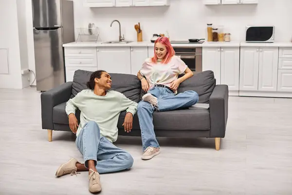 Appealing joyful multiracial couple in homewear sitting in living room and smiling at each other — Stock Photo