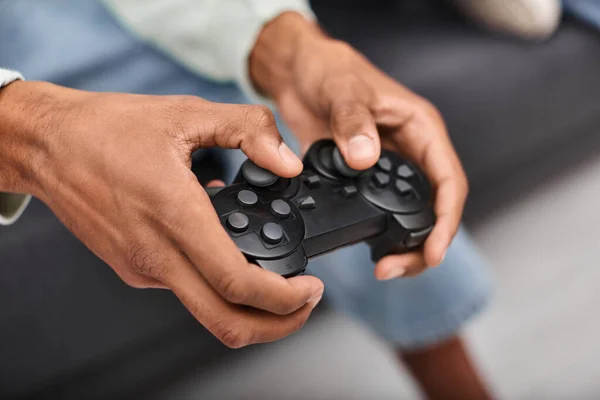 Vista ritagliata del gamepad moderno nelle mani di un giovane uomo afroamericano che gioca in salotto — Foto stock
