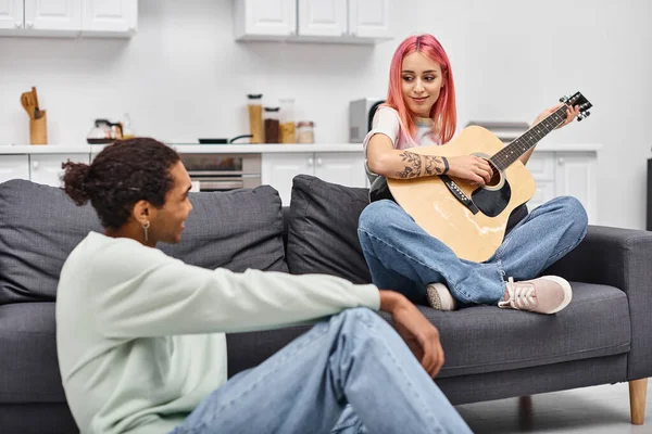 Pink haired beautiful woman playing guitar and looking at her loving african american boyfriend — Stock Photo