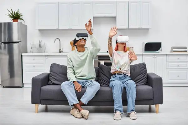 Красивая веселая межрасовая пара сидит на диване в гостиной дома с VR гарнитурами — стоковое фото