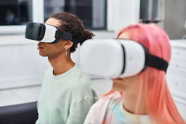 Se centran en el hombre afroamericano junto a la novia de pelo rosa borrosa con auriculares de realidad virtual - foto de stock