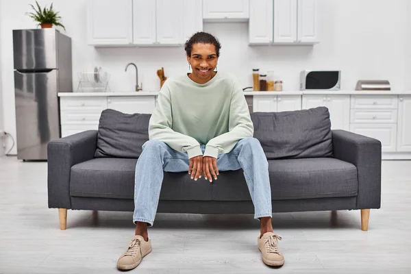 Joyful young african american man in comfy homewear sitting on sofa and looking at camera at home — Stock Photo