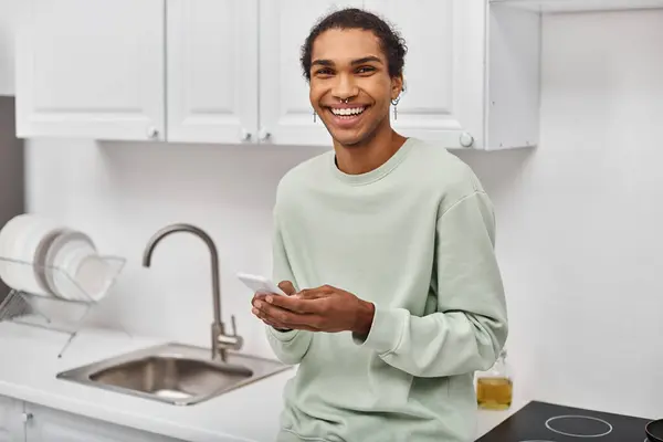 Atraente homem americano africano alegre em roupas confortáveis segurando smartphone e sorrindo para a câmera — Fotografia de Stock