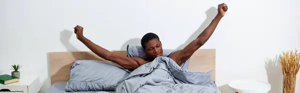 Ein junger afroamerikanischer Mann liegt im Bett und streckt nach dem Aufwachen am Morgen die Arme in die Luft. — Stockfoto