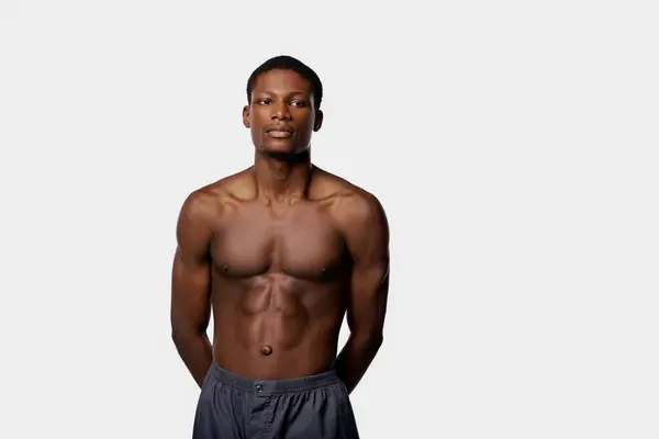 A muscular African American man stands shirtless in a studio with a white background, showcasing his physique. — Stock Photo