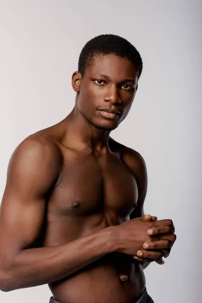 A shirtless African American man poses stylishly in a studio against a white background during a beauty routine. — Stock Photo