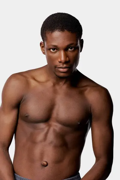 A shirtless African American man poses gracefully in a studio against a white backdrop during his beauty routine. — Stock Photo