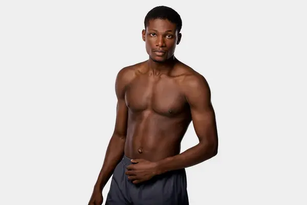 Shirtless uomo afroamericano si erge con fiducia contro uno sfondo bianco crudo. — Foto stock