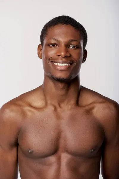 A shirtless African American man strikes a pose in a studio against a white backdrop, executing his beauty routine. — Stock Photo