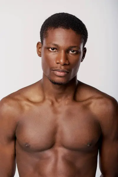 A shirtless African American man strikes a pose in a studio with a white background for a beauty routine session. — Stock Photo