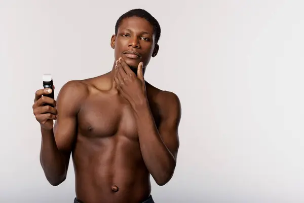 An African American man, shirtless, holding electric razor in a serene studio setting against a white backdrop. — Stock Photo