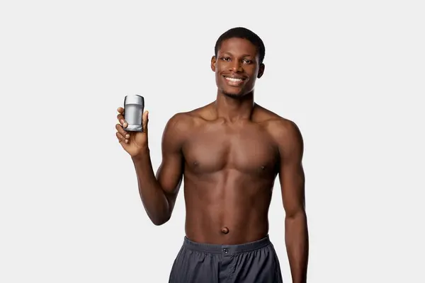 An African American man in a studio, shirtless, holding deodorant — Stock Photo