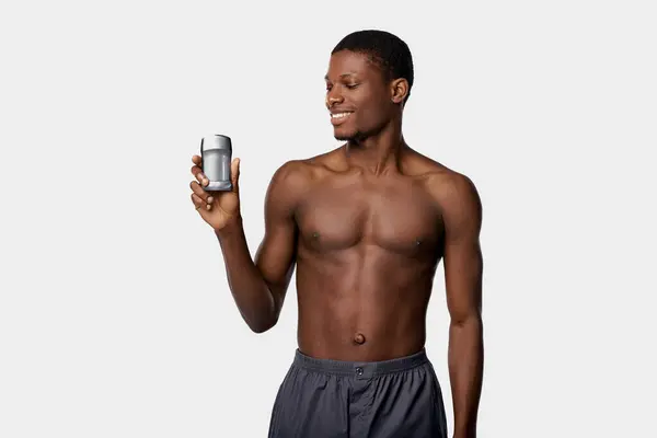 A shirtless African American man holding a can of beer and a cell phone in a studio with a white background. — Stock Photo