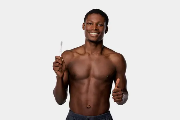 Shirtless uomo afroamericano tiene uno spazzolino da denti nella mano destra su uno sfondo bianco studio. — Foto stock