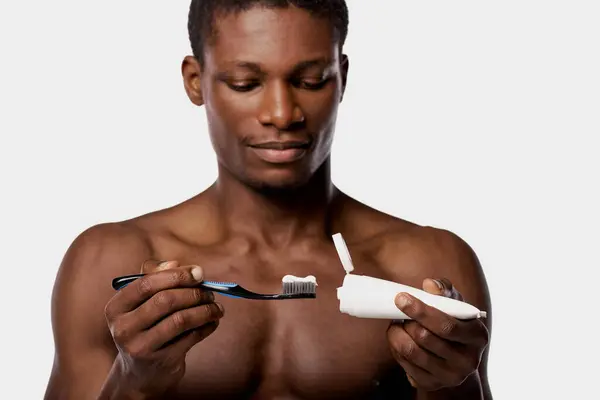 Shirtless African American man in studio with white background, holding a toothbrush and an toothbrush. — Stock Photo