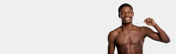 Ein Afroamerikaner ohne Hemd putzt sich in einem Studio vor weißem Hintergrund die Zähne. — Stockfoto