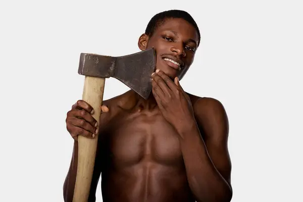A shirtless African American man confidently shaving with large axe in a striking pose against a white backdrop. — Stock Photo