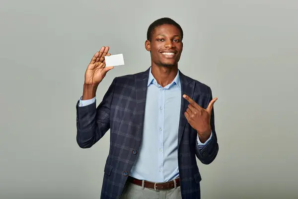 Handsome African American businessman in a suit with checkered blazer holding a business card against a grey backdrop. — Stock Photo