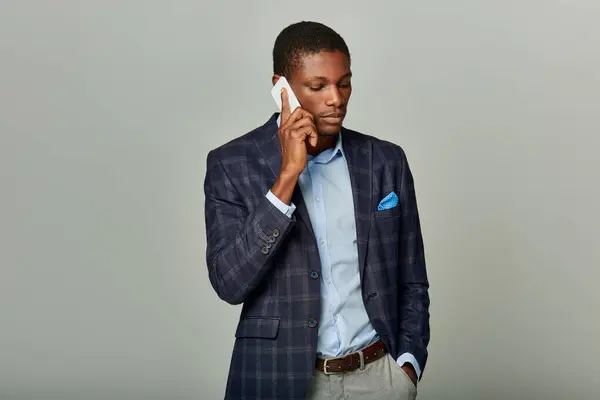 A young African American businessman in a checkered blazer is engaged in a phone conversation, exuding professionalism. — Stock Photo