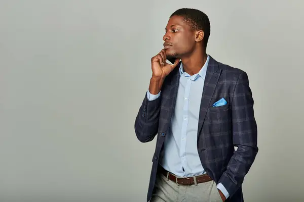 Handsome African American businessman in checkered blazer poses confidently in formal attire on a grey background. — Stock Photo