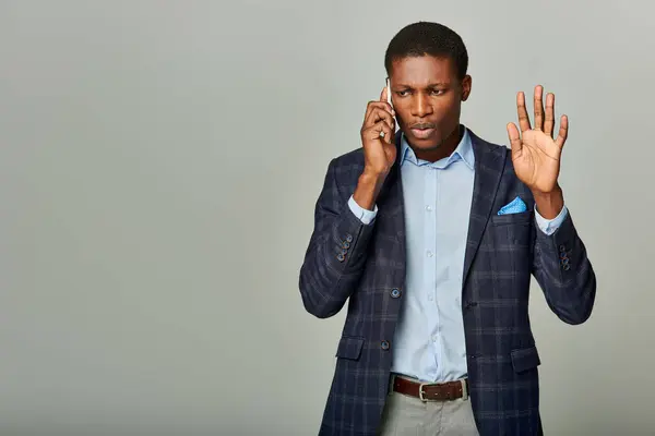 Young African American man in checkered suit speaking on cellphone against grey backdrop. — Stock Photo