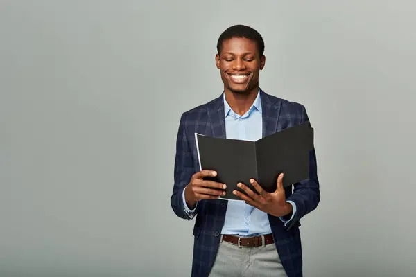 Stylish African American businessman in checkered blazer holding a folder on a grey background. — Stock Photo