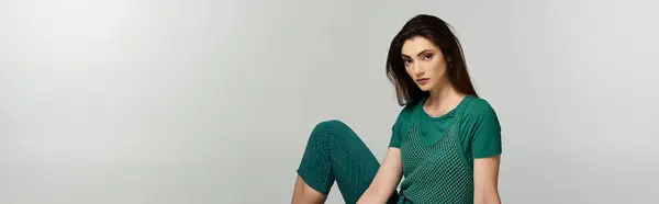 Uma jovem se senta em uma roupa verde elegante contra um pano de fundo branco. — Fotografia de Stock