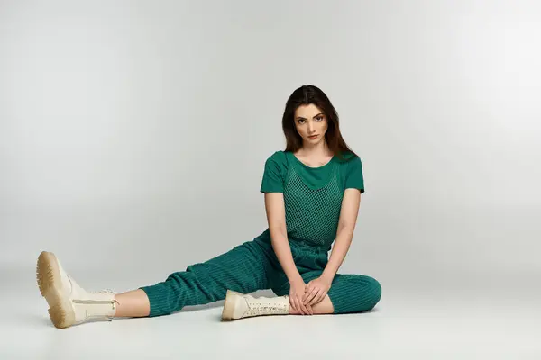 A young woman in a green outfit sits gracefully on a white background, showcasing her elegant style. — Stock Photo