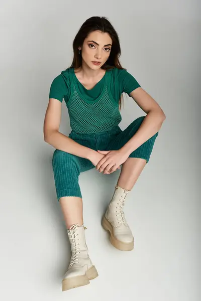 A young woman sits on a white backdrop, wearing an elegant green outfit. — Stock Photo