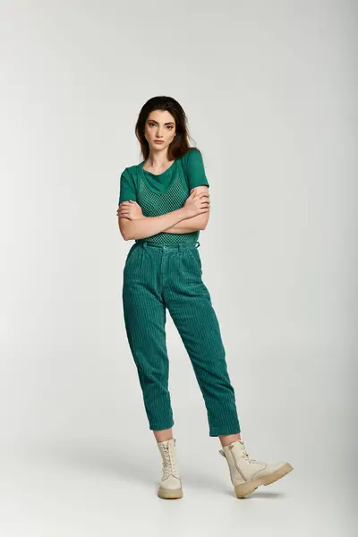 A young woman poses with her arms crossed, wearing emerald green corduroy pants and a green shirt. — Stock Photo