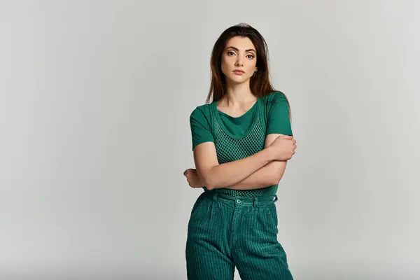 A young woman in a green outfit poses against a light grey background. — Stock Photo
