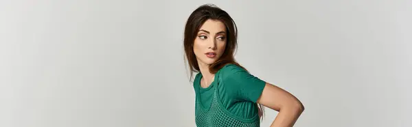 A young woman with long brown hair poses in a green mesh top against a white backdrop. — Stock Photo