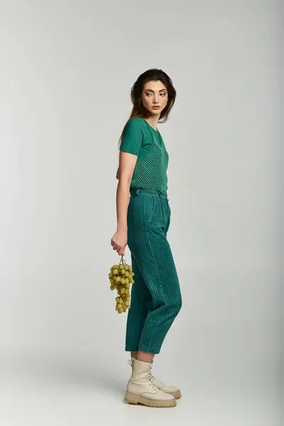 A woman in green pants and a green shirt holding a bunch of grapes. — Stock Photo