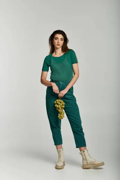 A young woman in a green outfit holds a bunch of grapes against a white background. — Stock Photo