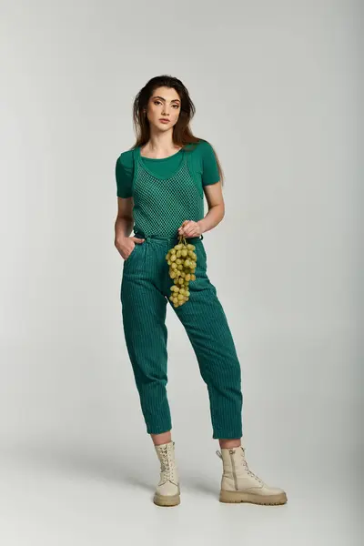 A young woman in a green outfit holds a bunch of grapes. — Stock Photo