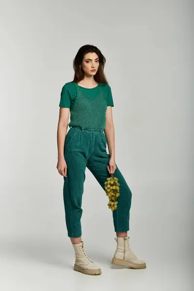 Eine junge Frau im grünen Outfit und weißen Stiefeln posiert mit Weintrauben. — Stock Photo
