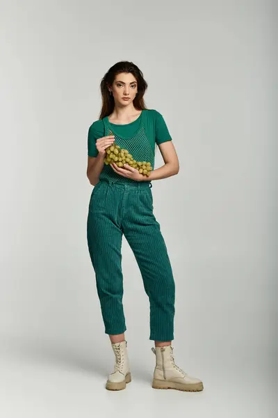 A young woman in a green outfit holds a bag of grapes. — Stock Photo